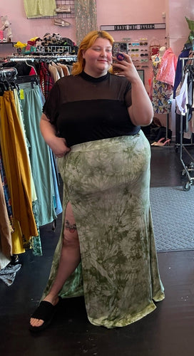 Full-body front view of a size 3X Fashion Nova green and white acid wash tie-dye maxi skirt with high high side slit and mini skirt lining styled with a black mesh-detail crop and black slides on a size 22/24 model.