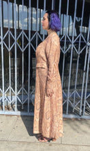 Load image into Gallery viewer, Full-body side view of a size 12 Mara Hoffman tan, brown, and white snake print button-up maxi dress with hip pocket details styled with snake print heels on a size 10 model. The photo is taken outside in natural lighting.
