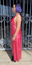 Load image into Gallery viewer, Full-body side view of a size 14 Dima Ayaad grapefruit pink colored v-neck gown with big sequins all throughout styled with black combat boots on a size 10 model. The photo is taken outside in natural lighting.
