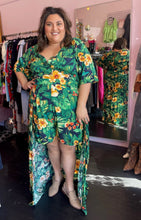 Load image into Gallery viewer, Additional full-body front view (with in-mirror view of the back) of a size 22/24 LTS (UK brand) kelly green, navy blue, and bright yellow tropical pattern romper with walk-through train detail styled with tan flats on a size 18/20 model.
