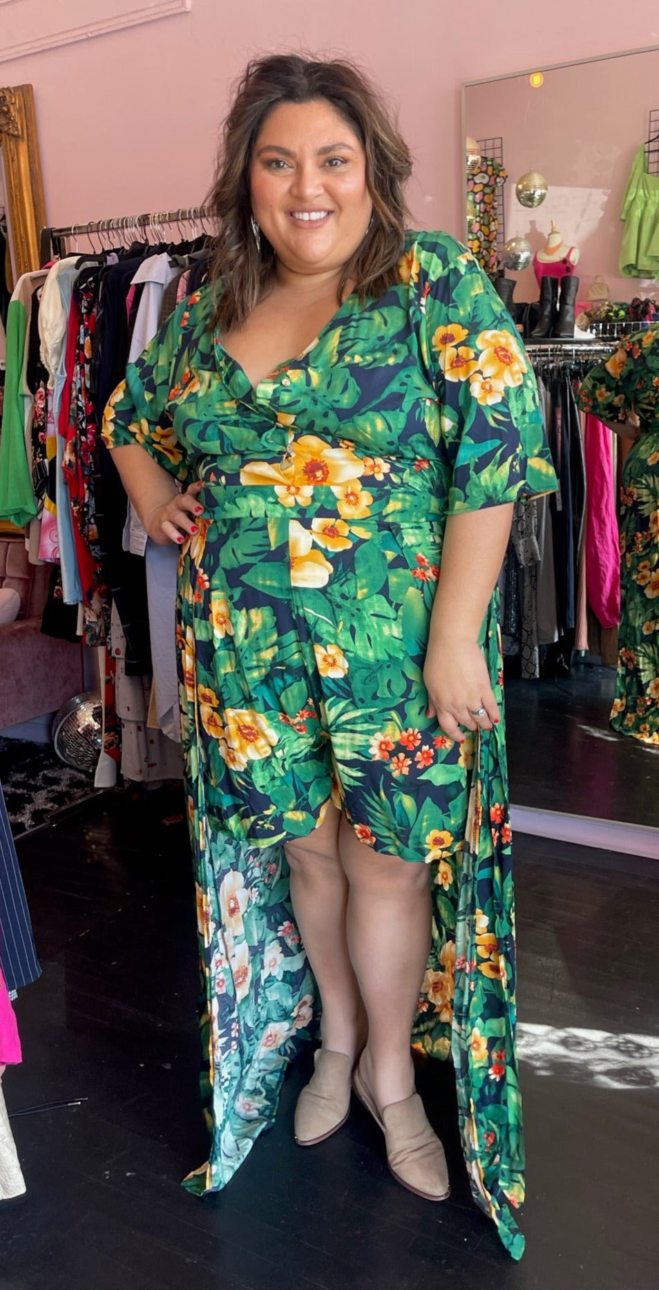 Full-body front view of a size 22/24 LTS (UK brand) kelly green, navy blue, and bright yellow tropical pattern romper with walk-through train detail styled with tan flats on a size 18/20 model.