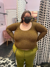 Load image into Gallery viewer, Additonal front view of a size XL (fits up to size 24) GANNI deep gold metallic ribbed knit sweater styled with olive green trousers on a size 24 model. The photo is taken inside in overhead lighting.
