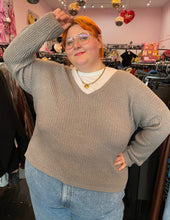 Load image into Gallery viewer, Front view showing off the sleeves of a size 4X Wild Fable gray-brown v-neck knit sweater styled over a white tee and lightwash denim on a size 22/24 model. The photo is taken inside under overhead lighting, which makes the tone of the sweater pull warmer.

