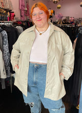 Load image into Gallery viewer, Additional front view of a size 2/3X Public Desire brand off-white faux leather longline snap button-up top styled open over a white cropped tee and lightwash denim on a size 22/24 model.
