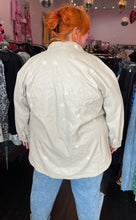 Load image into Gallery viewer, Back view of a size 2/3X Public Desire brand off-white faux leather longline snap button-up top styled open over a white cropped tee and lightwash denim on a size 22/24 model.
