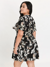 Load image into Gallery viewer, Back view of a black, white, and cream floral mini dress with ruffles at the sleeves.
