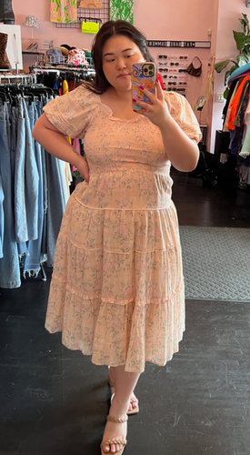 Full-body front view of a size L Ivy City blush pink tiered midi dress with mini ruffles, puff sleeves, and a smocked bust styled with tan heels on a size 14/16 model.